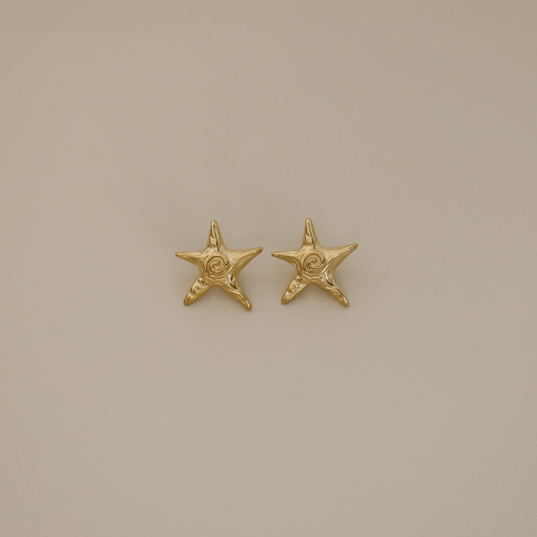 estarlin earrings, gold irregular medium star-shaped studs with a whimsical design. Each earring features a raised swirl at the center and touches of irregular textures placed throughout