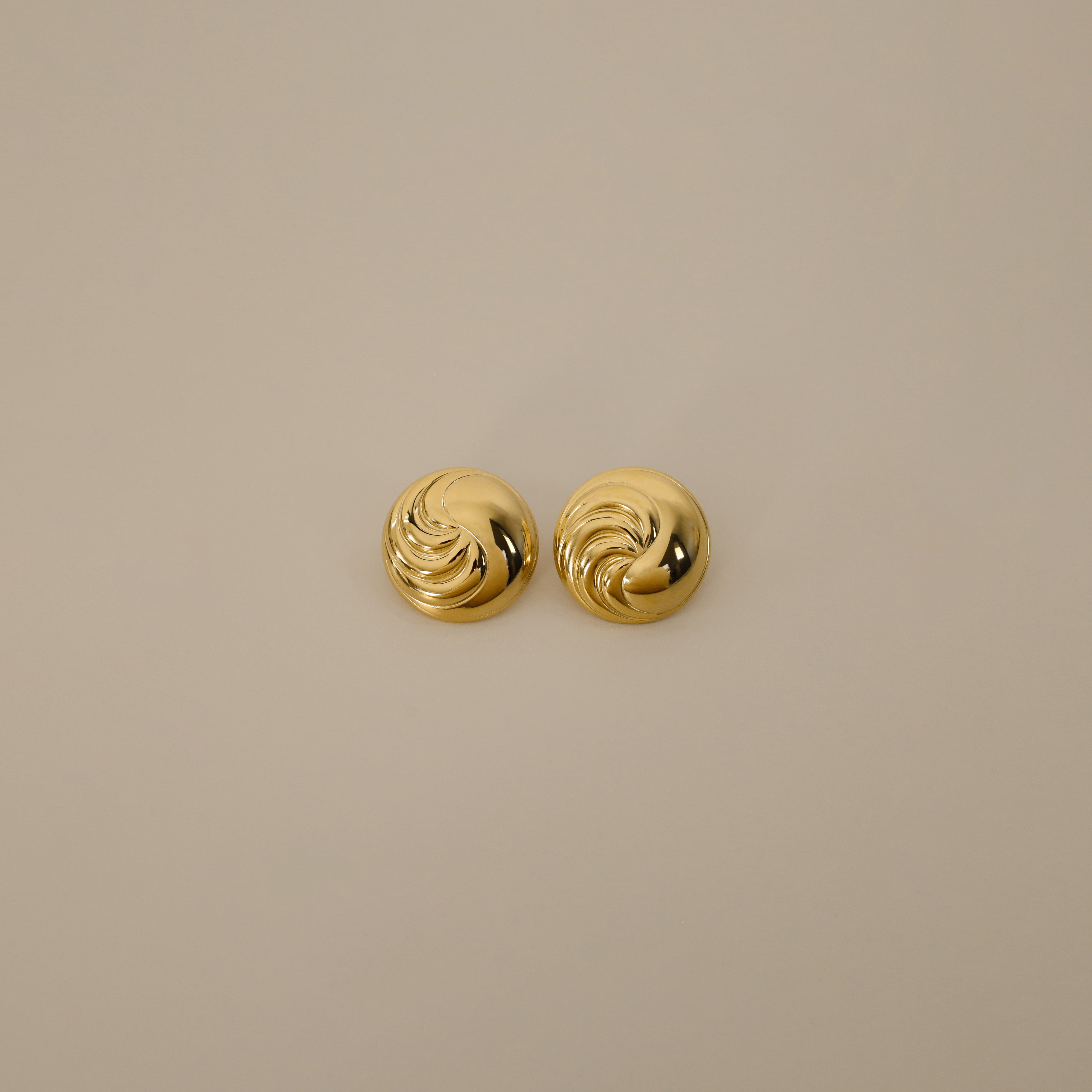 erlik earrings, gold bold circular design with a swirling pattern on one half of the earring and a smooth polished finish on the other half