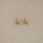 estarlin earrings, gold irregular medium star-shaped studs with a whimsical design. Each earring features a raised swirl at the center and touches of irregular textures placed throughout