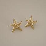 estarlin earrings, gold irregular medium star-shaped studs with a whimsical design. Each earring features a raised swirl at the center and touches of irregular textures placed throughout