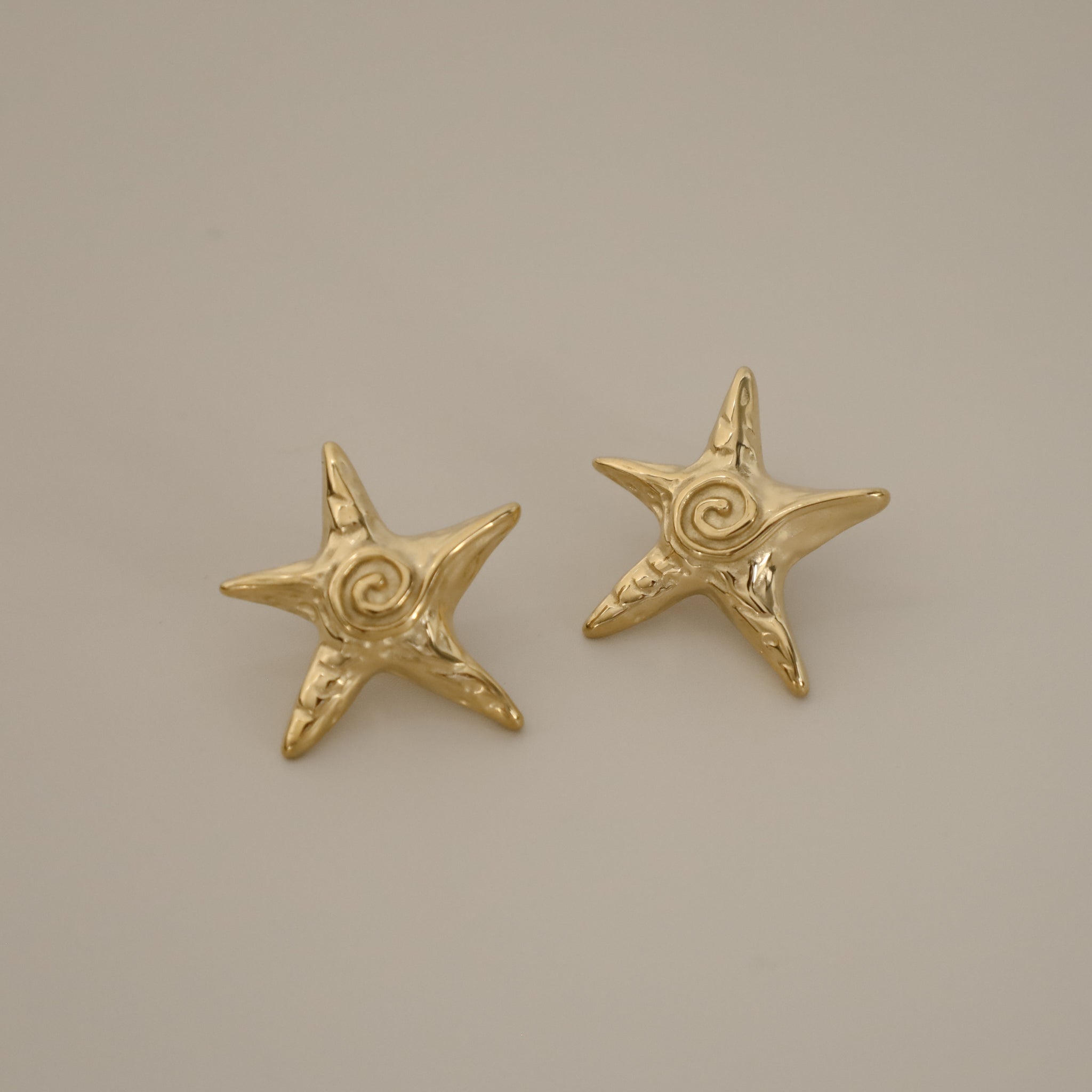 estarlin earrings, gold irregular medium star-shaped studs with a whimsical design. Each earring features a raised swirl at the center and touches of irregular textures placed throughout