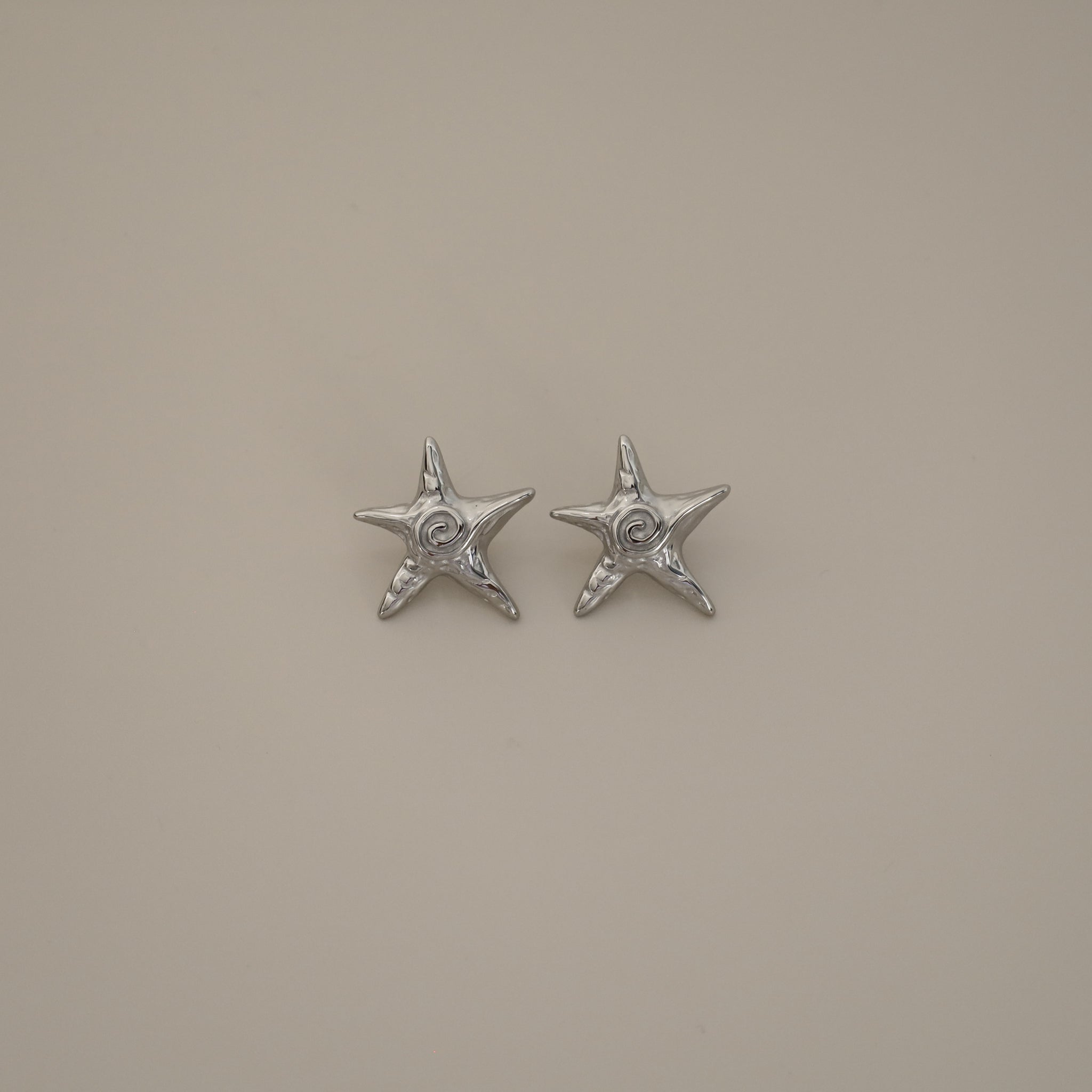 estarlin earrings, silver irregular medium star-shaped studs with a whimsical design. Each earring features a raised swirl at the center and touches of irregular textures placed throughout