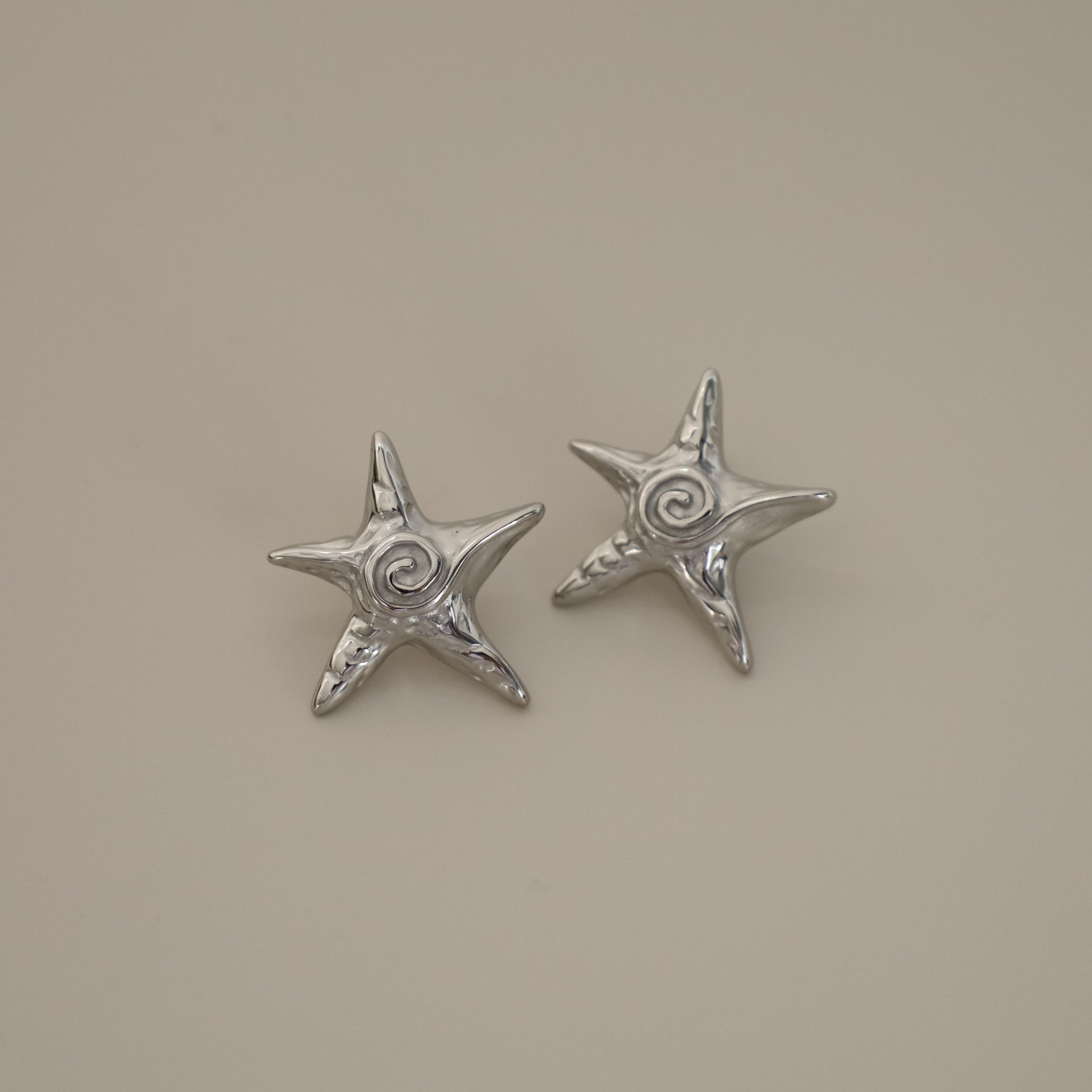 estarlin earrings, silver irregular medium star-shaped studs with a whimsical design. Each earring features a raised swirl at the center and touches of irregular textures placed throughout