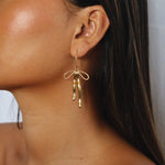 erkinne gold earrings, delicate bow design with dangling ribbons on model