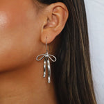 erkinne silver earrings, delicate bow design with dangling ribbons on model