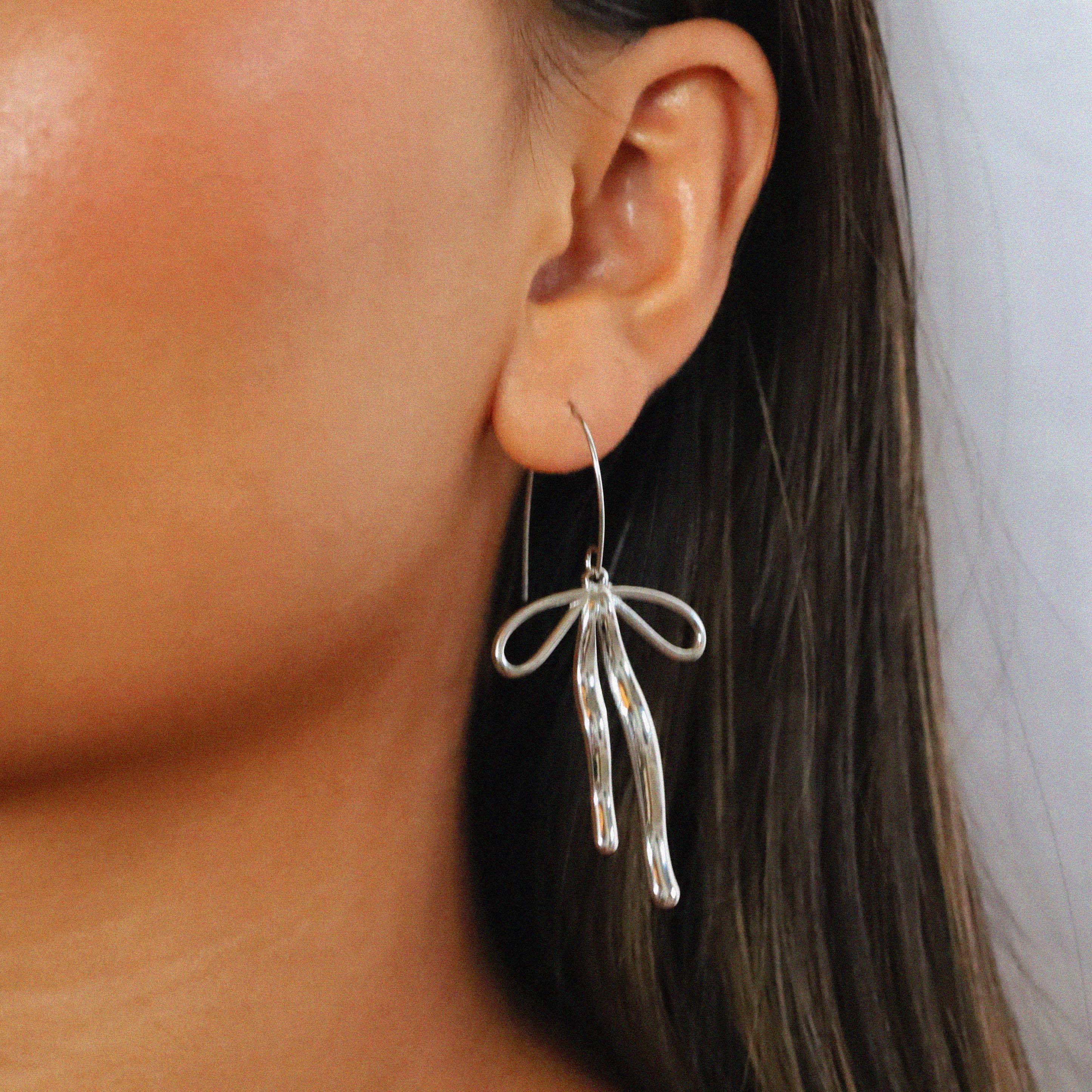 erkinne silver earrings, delicate bow design with dangling ribbons on model