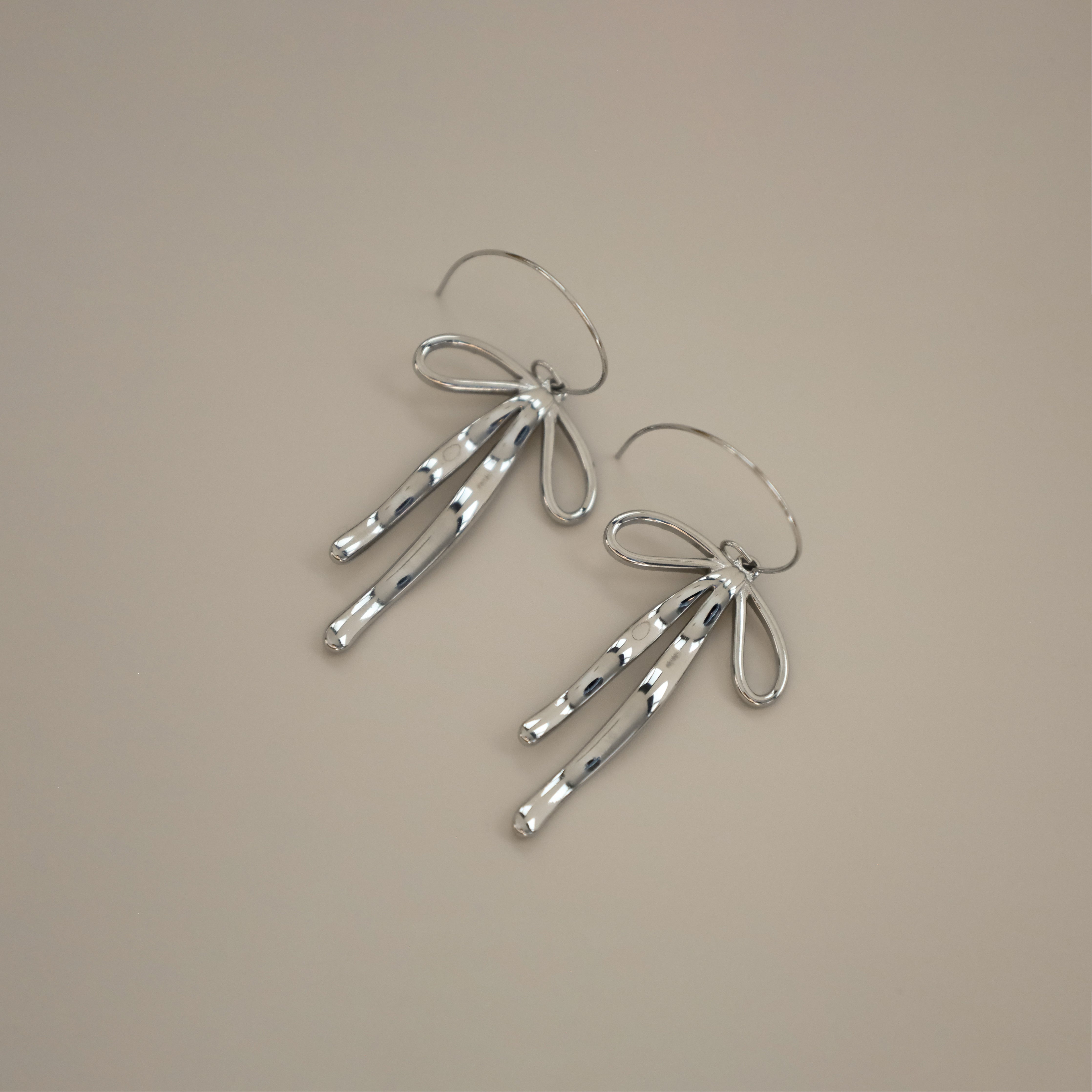 erkinne silver earrings, delicate bow design with dangling ribbons on model