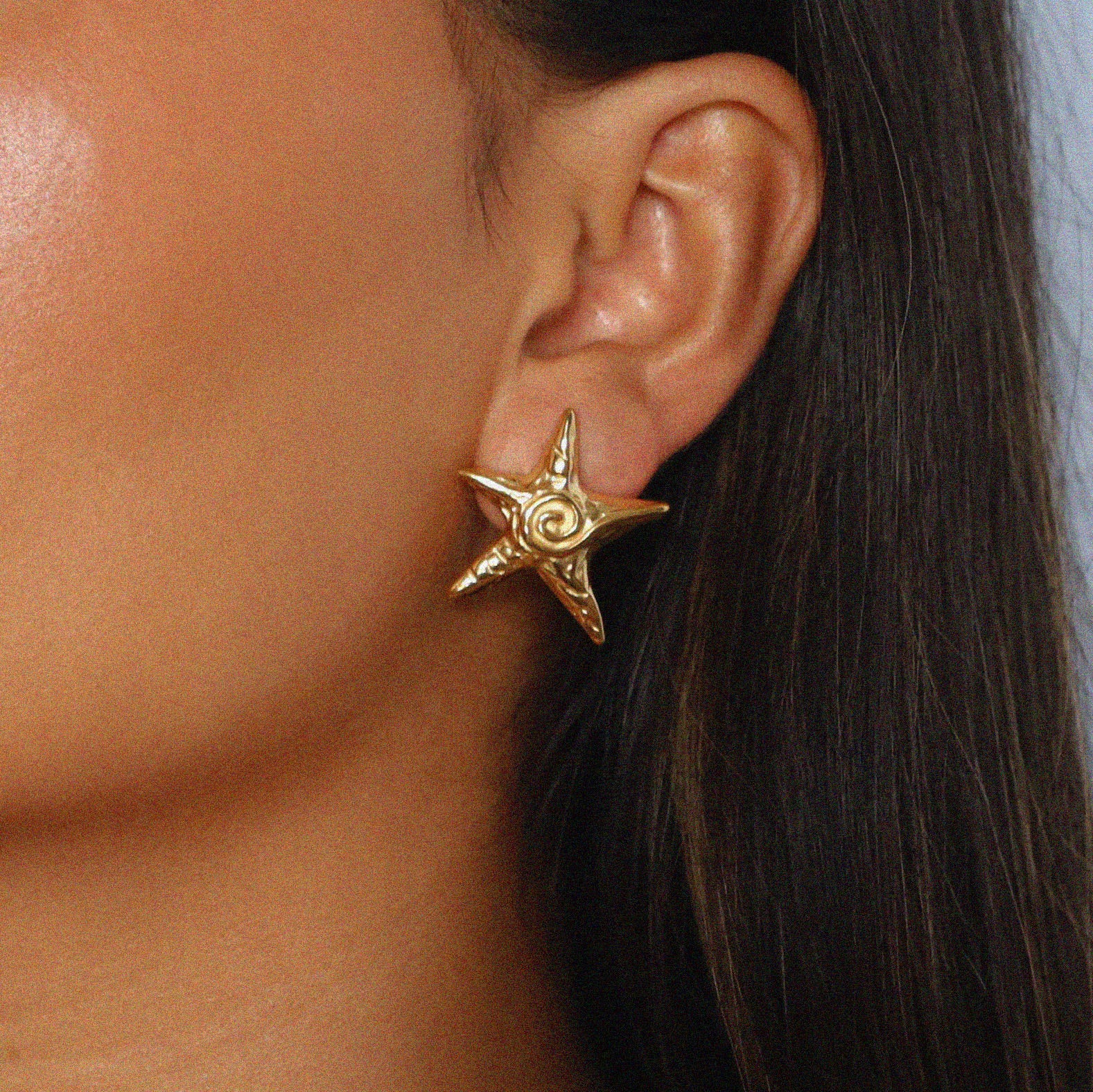 estarlin earrings, gold irregular medium star-shaped studs with a whimsical design. Each earring features a raised swirl at the center and touches of irregular textures placed throughout