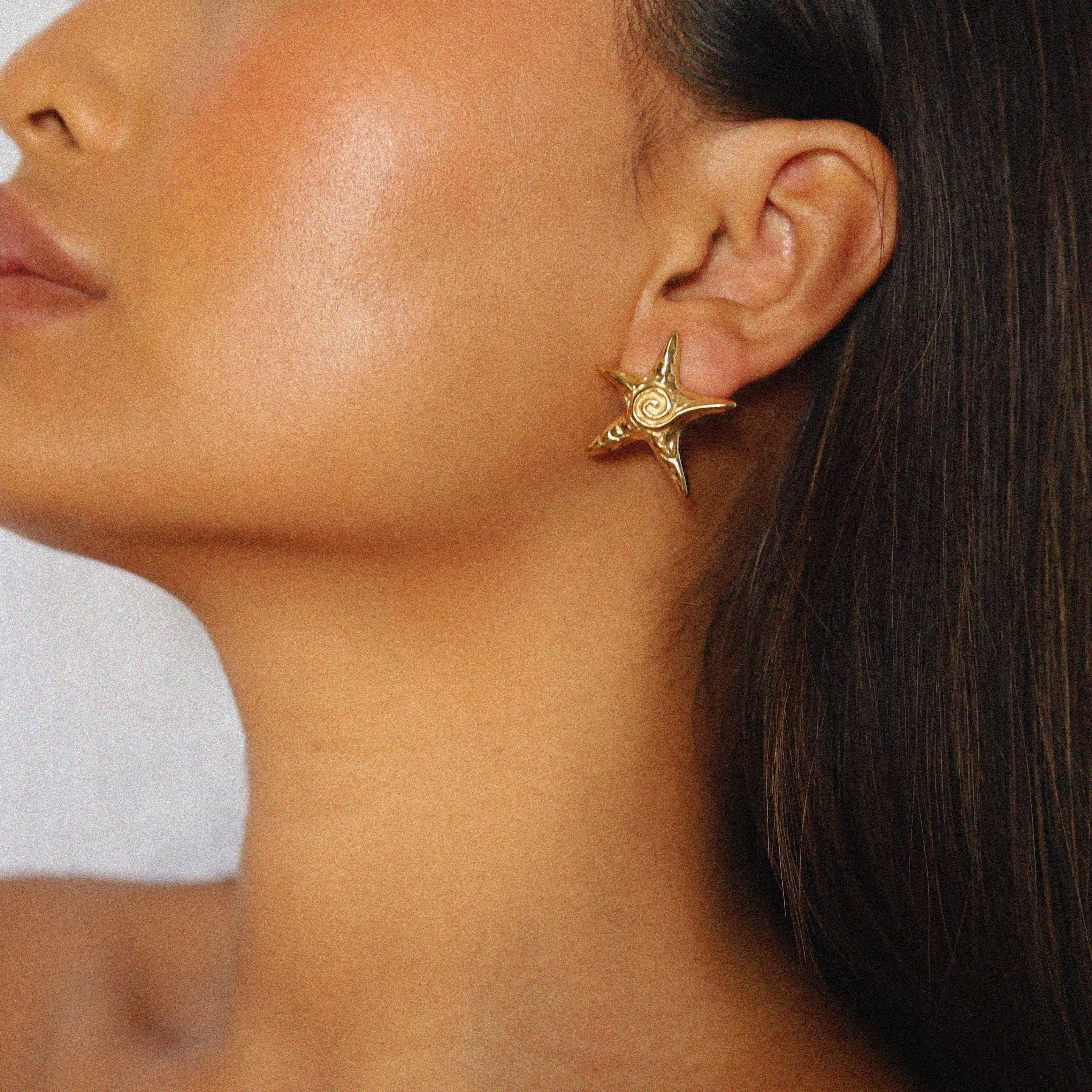 estarlin earrings, gold irregular medium star-shaped studs with a whimsical design. Each earring features a raised swirl at the center and touches of irregular textures placed throughout