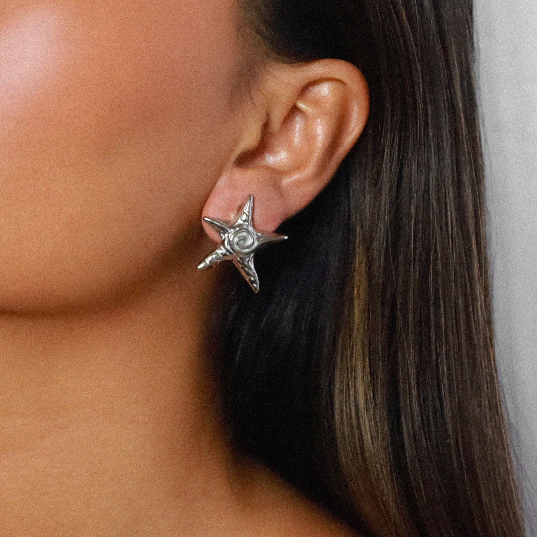 estarlin earrings, silver irregular medium star-shaped studs with a whimsical design. Each earring features a raised swirl at the center and touches of irregular textures placed throughout